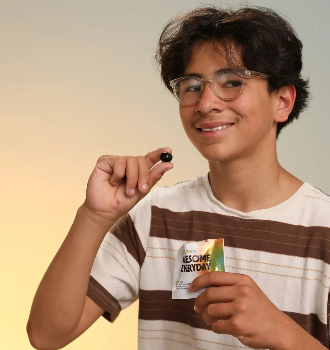  Smiling child holding an Awesome Everyday Kids & Teens packet and a gummy in another hand.