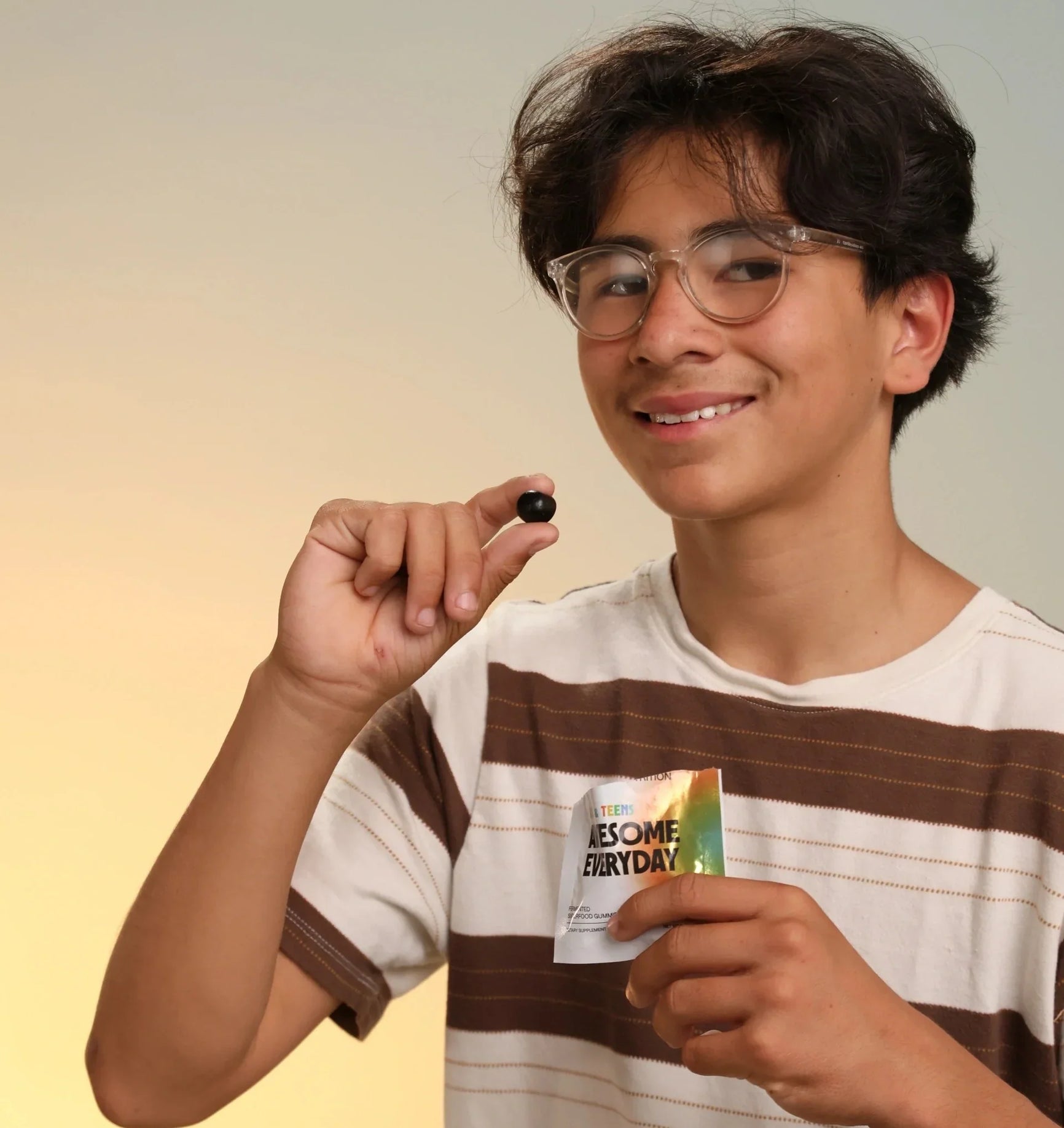  Smiling child holding an Awesome Everyday Kids & Teens packet and a gummy in another hand.
