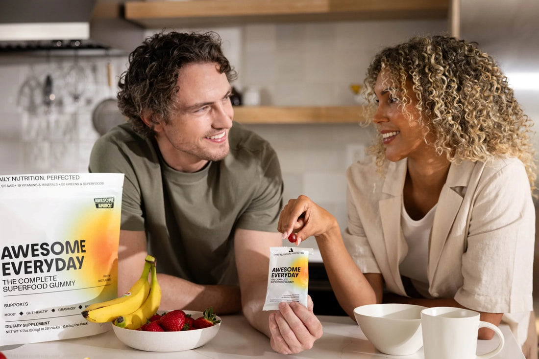Man and woman sharing Awesome Everyday gummies in a kitchen with fruit and coffee nearby.