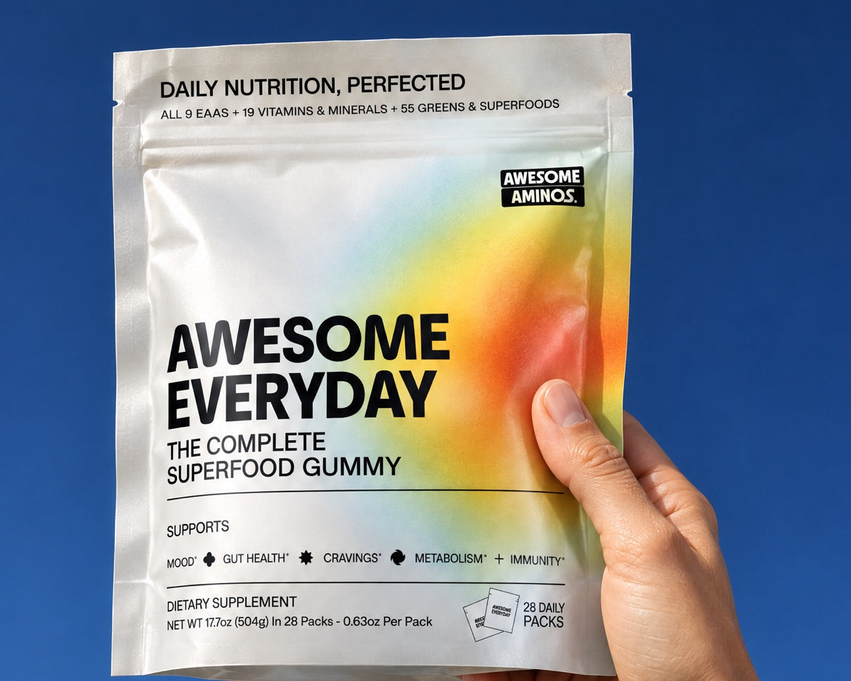 A hand holding a pouch of Awesome Everyday up against a blue sky