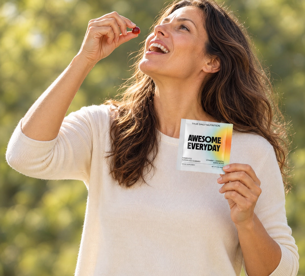 A smiling woman outdoors eating an Awesome Everyday gummy