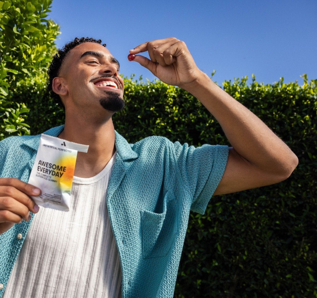 A smiling man holding a daily pack of Awesome Everyday and eating a gummy